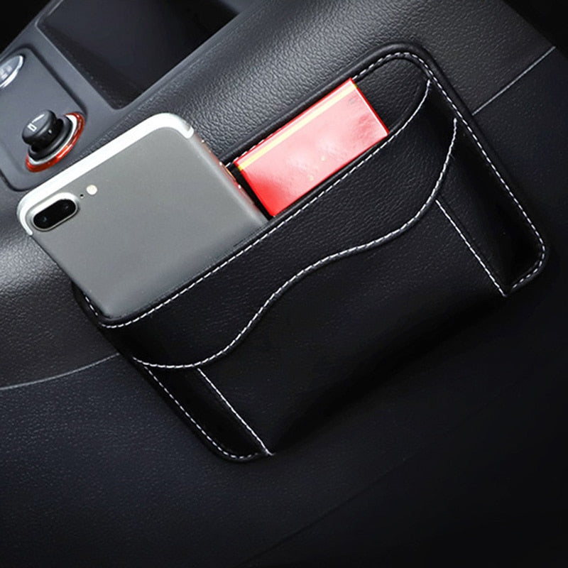 Black nylon car organizer box bag on an air vent, storing a phone and cards in a vehicle interior.