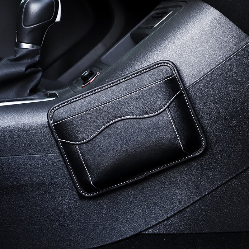 Black nylon car organizer box bag on an air vent, storing a phone and cards in a vehicle interior.
