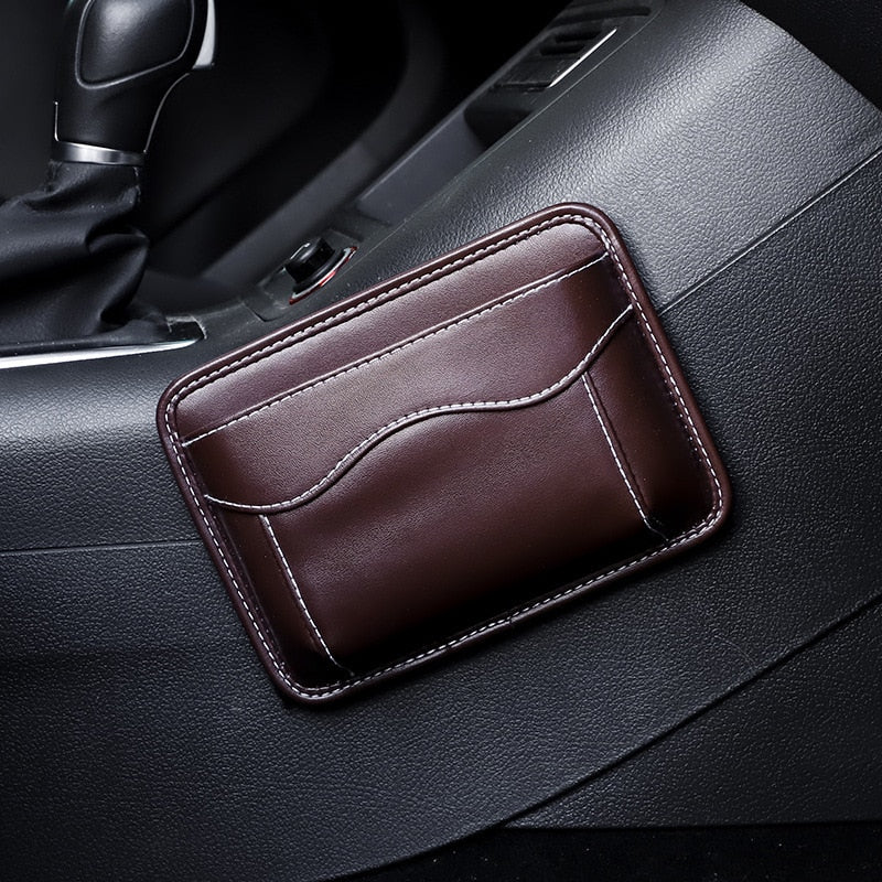Black nylon car organizer box bag on an air vent, storing a phone and cards in a vehicle interior.
